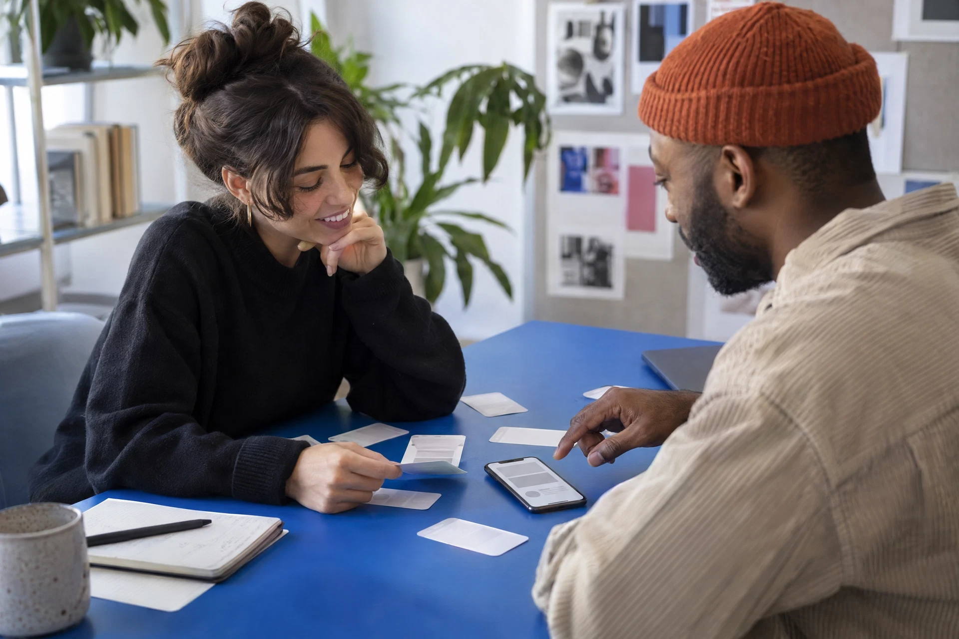 Two people reviewing a generic phone prototype and blank flow cards at a blue table